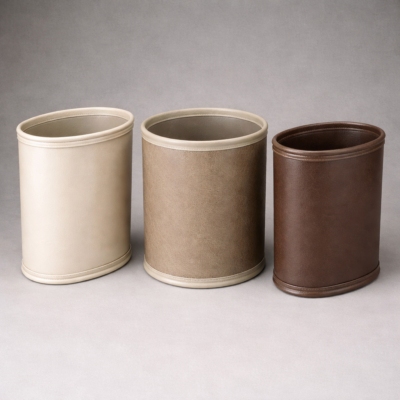 Oval leatherette wastebasket with textured faux leather finish, designed for hotel guest rooms, bathrooms, and offices.